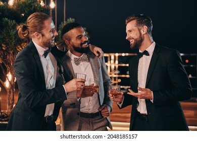 Three handsome men in suits drinking whiskey and communicating while spending time on party - Powered by Shutterstock