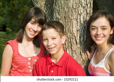Three happy adolescents standing by a tree in the afternoon sun.