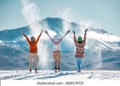 Drei glückliche erwachsene Mädchen haben Spaß und werfen ersten Schnee auf den Hintergrund der Berge. Winterzeitkonzept für Reisen