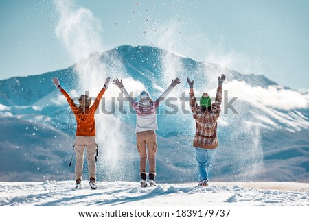 Three happy adult girls are having fun and throws first snow on background of mountains. Travel in winter time concept