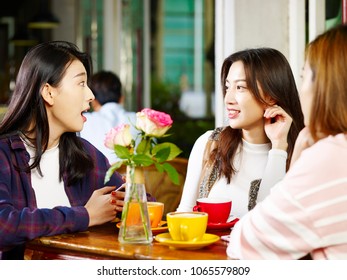 three happy beautiful young asian women sitting at table chatting talking in coffee shop or tea house. - Shutterstock ID 1065579809