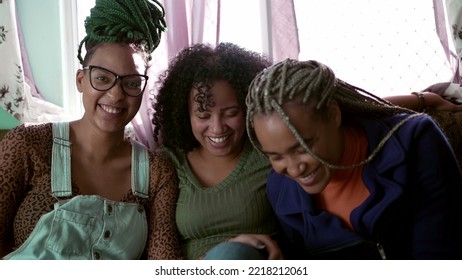 Three happy carefree Brazilian young black women laughing and smiling. Happy hispanic people authentic real life laugh and smile hanging at home looking at camera Stock Photo