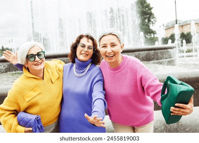 Three happy cheerful pensioner female friends in bright sweaters and sunglasses walk together. Lifestyle and people concept. - Powered by Shutterstock