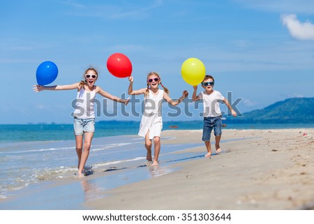 Three Happy Children With Balloons Running On The Beach At The Day Time Concept Of Three Happy Children With Balloons Running On The Beach At The Day Time Concept Of