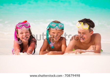 	Three happy children on beach with colorful face masks and snorkels, sea in background.