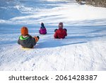 Three happy children on a hill with plastic shovel sleds.