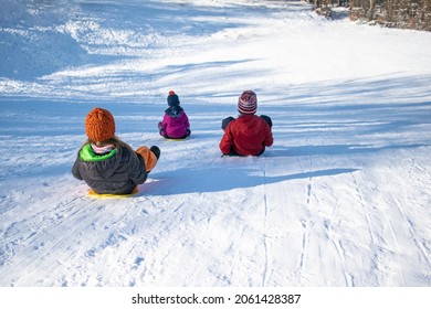 Three happy children on a hill with plastic shovel sleds.
