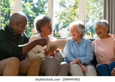 Three happy diverse senior woman and african american male friend sitting on sofa and using tablet. retirement lifestyle relaxing at home with technology.