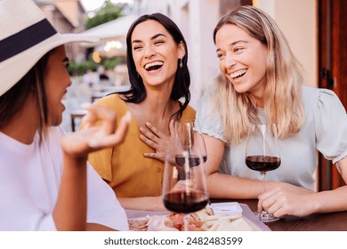 Three happy diverse women having fun enjoying aperitif with red wine sitting at an outside table in a bar. Food and beverage concept. - Powered by Shutterstock