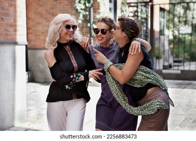 Three happy female friends laughing and cuddling outside. Lifestyle women portrait on city street - Powered by Shutterstock