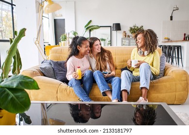 Three Happy Female Friends Smiling And Having Fun At Home - Funny Women Together Celebrating Sitting On The Living Room Sofa Drinking Juice And Coffee