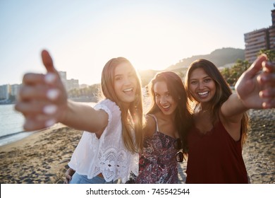 Three happy female friends standing on beach raising hands - Shutterstock ID 745542544