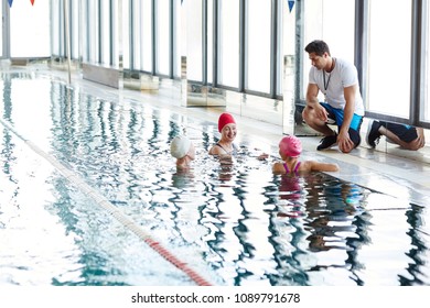 Three happy females in swimwear having talk in water while their trainer consulting them - Powered by Shutterstock