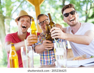 Three Happy Friends Drinking Beer, Chatting And Having Fun In Pub Garden