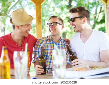 Three Happy Friends Drinking Beer, Chatting And Having Fun In Pub Garden