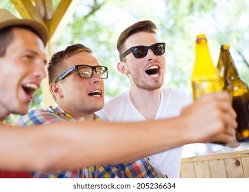 Three Happy Friends Drinking Beer, Chatting And Having Fun In Pub Garden