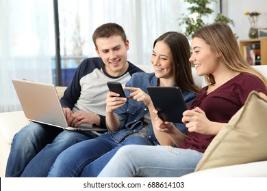 Three happy friends sharing on line content with multiple devices sitting on a sofa at home