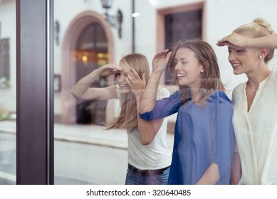 Three Happy Girl Friends At The Street Looking What Is Inside The Store Through Glass Window.