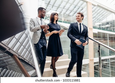 Three Happy Multiracial Business People Walking Down On Stairs Together With Digital Tablet