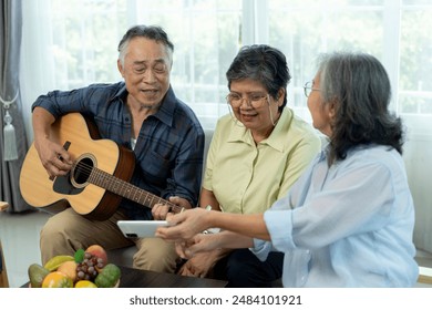 Three happy senior friends gathered indoors, one playing acoustic guitar while the others sing animatedly, female friend use smartphone photographing, enjoying music with camaraderie in living room. - Powered by Shutterstock