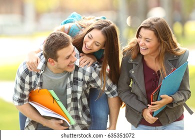 Three Happy Students And Friends Joking And Laughing Together In An University Campus With A Green Background