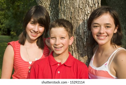 Three happy teens or pre-teens standing by a tree in the late afternoon sun.