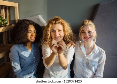 Three Happy Women Holding Hands In The Form Of Heart Multi Ethnic Friends Sitting Beside And Chatting In Restaurant During Lunch. Multi-racial, Difference Cultures Friendship Concept.