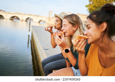 Three happy women sitting on the lakeside of the city eating pizza in a street stall. The happy girls enjoy the weekend together outdoors. - Powered by Shutterstock