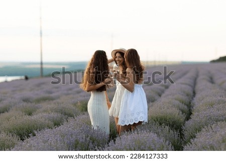 Three happy women in white dresses standing in lavender field on summer sunny day.