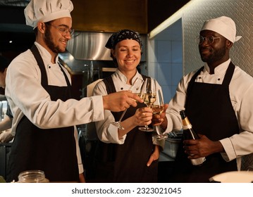 Three happy young intercultural cooks celebrating life event with champagne - Powered by Shutterstock