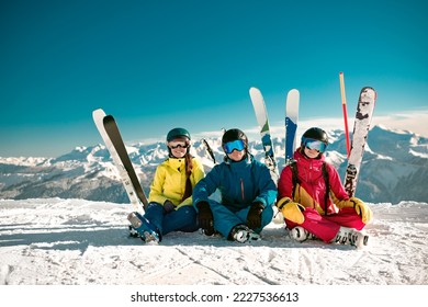 Three happy young skiers sits at mountain top and smiles. Winter vacations concept at ski resort - Powered by Shutterstock