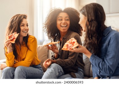 Three happy young women friends enjoying pizza together and chatting sitting on couch at home. Millennial ladies talking and laughing on weekend, savoring tasty junk food - Powered by Shutterstock