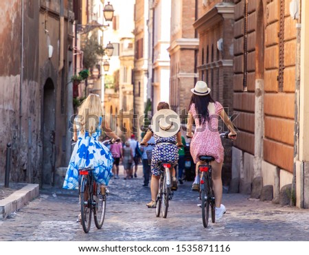 Three happy young women friends tourists with bikes in typical alley in Rome, Italy at sunrise.
