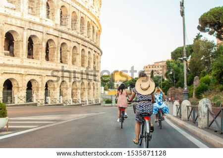 Three happy young women friends tourists with bikes at Colosseum in Rome, Italy at sunrise.