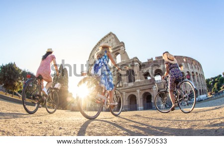 Three happy young women friends tourists with bikes at Colosseum in Rome, Italy at sunrise.