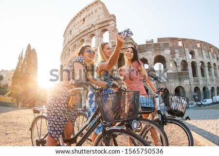 Three happy young women friends tourists with bikes taking selfies at Colosseum in Rome, Italy at sunrise.