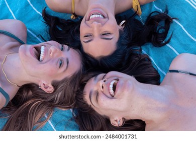 Three happy young women sunbathing on beach towels on the sand - Powered by Shutterstock