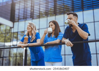 Three healthcare professionals wearing scrubs enjoy a coffee break outdoors, leaning on a railing and sharing a lighthearted moment in a modern urban setting. - Powered by Shutterstock