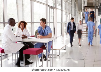 Three healthcare workers talking in a busy modern lobby