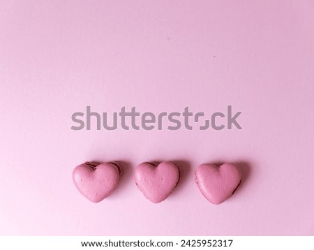 Three heart shaped pink macaron cookies on bright pink background