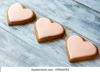 Three heart-shaped cookies. Biscuits with light pink glaze. Lots of love. Sweet treats for loved ones.