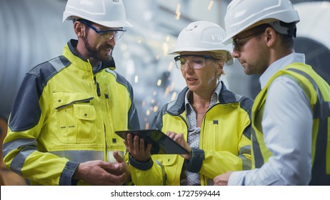 Three Heavy Industry Engineers Stand in Pipe Manufacturing Factory  Use Digital Tablet Computer  Have Discussion  Large Pipe Assembled  Design   Construction Oil  Gas   Fuels Transport Pipeline