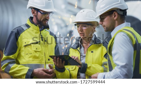 Three Heavy Industry Engineers Stand in Pipe Manufacturing Factory, Use Digital Tablet Computer, Have Discussion. Large Pipe Assembled. Design and Construction of Oil, Gas and Fuels Transport Pipeline 商業照片 © 