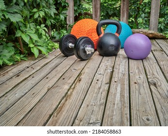 three heavy slam balls, iron kettlebell and dumbbell on a backyard deck, home and backyard gym concept