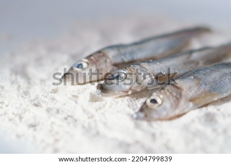 Three herrings on a plate with flour. Stages of cooking fish. Preparation for frying food. Home kitchen.