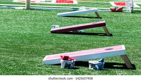 Three homeaide wooden corn hole game boards are set up side by side on a green turf field with bean bags in containers.