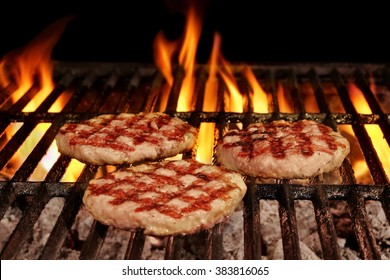 Three Homemade Browned Burgers On The Hot Flaming BBQ Charcoal Grill With Bright Flames On The Black Background, Overhead  View, Cookout Food For Outdoor Party Or Picnic