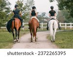 Three horsewomen enjoy riding beautiful horses, side by side along the trail at the equestrian center on a sunny day