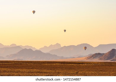 Three Hot Air Balloons Fly Over The Namib Desert During Sunrise.  Namibia