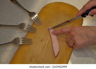 Three Hungry Forks On A Wooden Cutting Board Near One Small Piece Of Meat Sausage With A Knife. Food Crisis, Food Shortage.